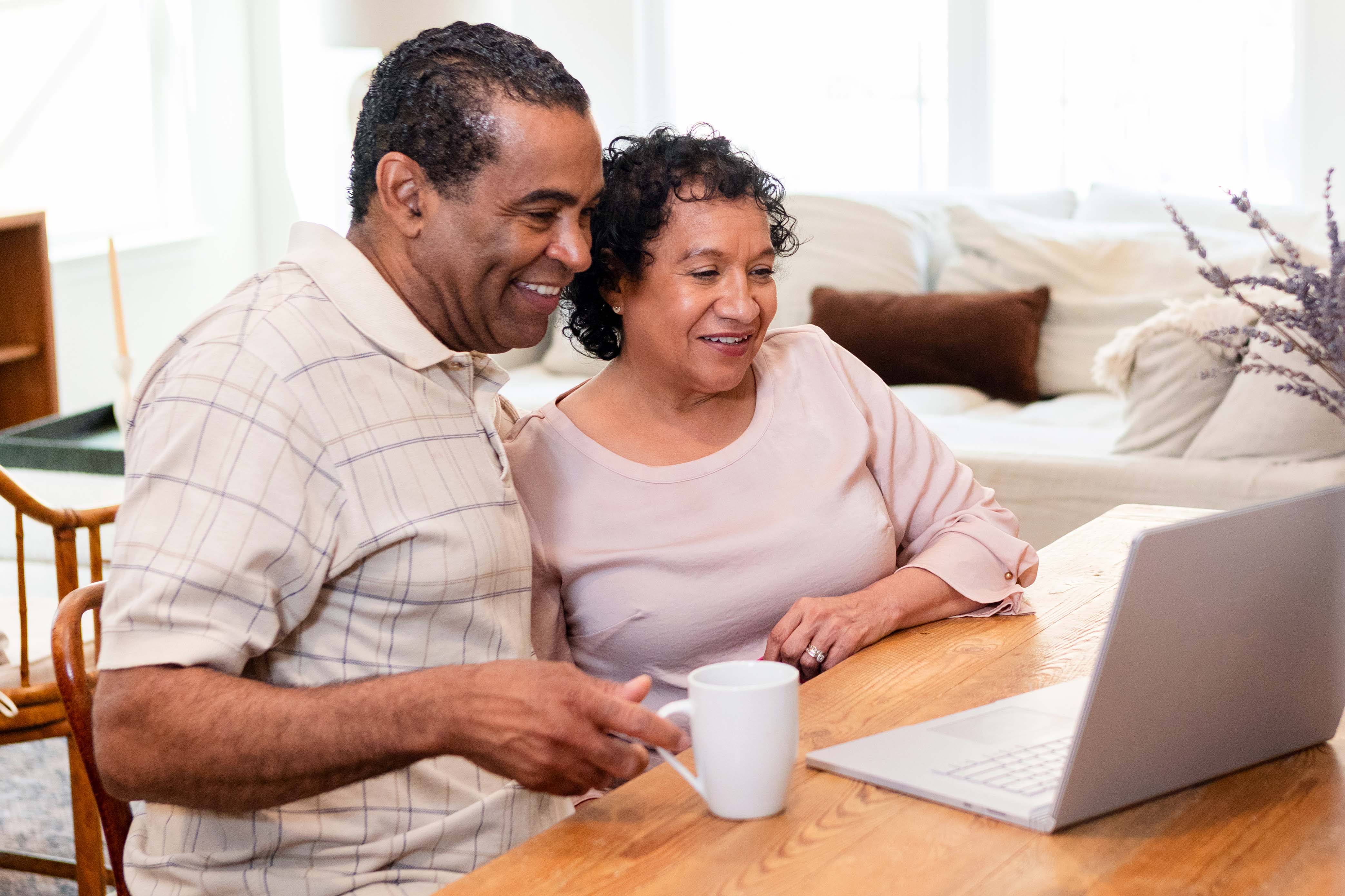 A mature couple reads the news on a computer while enjoying a cup of coffee.